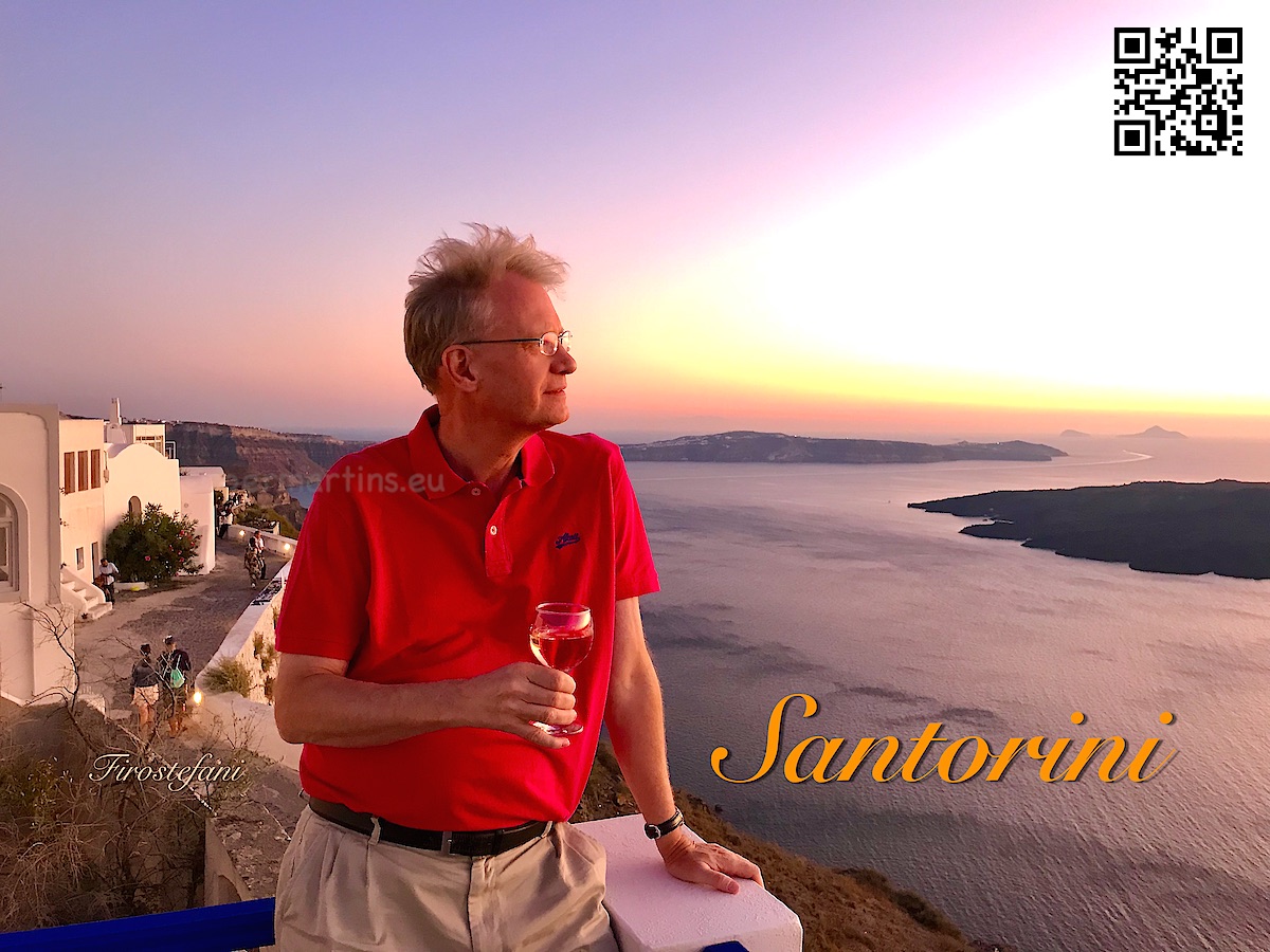 Greece Santorini Firostefani man holding a drink and looking out over the caldera at sunset